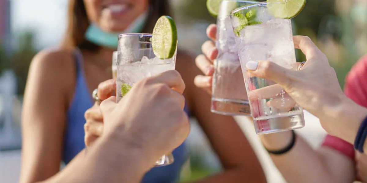 friends drinking cocktails in an outdoors snack bar restaurant in the summer wearing face mask on to be protected from coronavirus - happy people cheering with mojito and having fun friends drinking cocktails in an outdoors snack bar restaurant in the summer wearing face mask on to be protected from coronavirus - happy people cheering with mojito and having fun