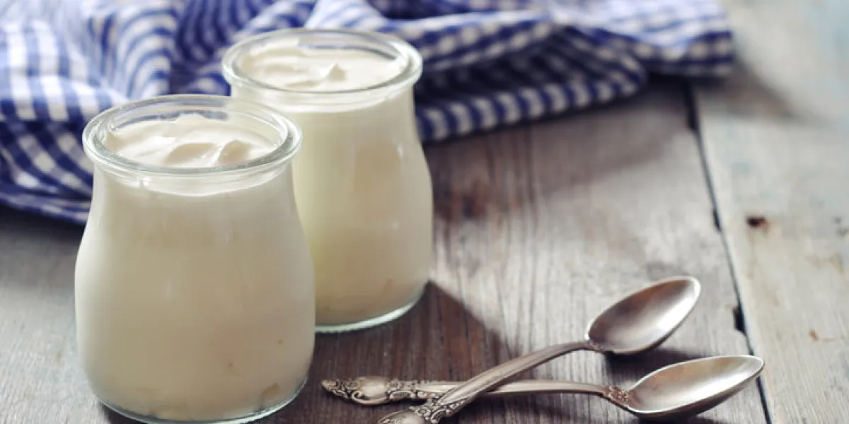 greek yogurt in a glass jars with spoons on wooden background