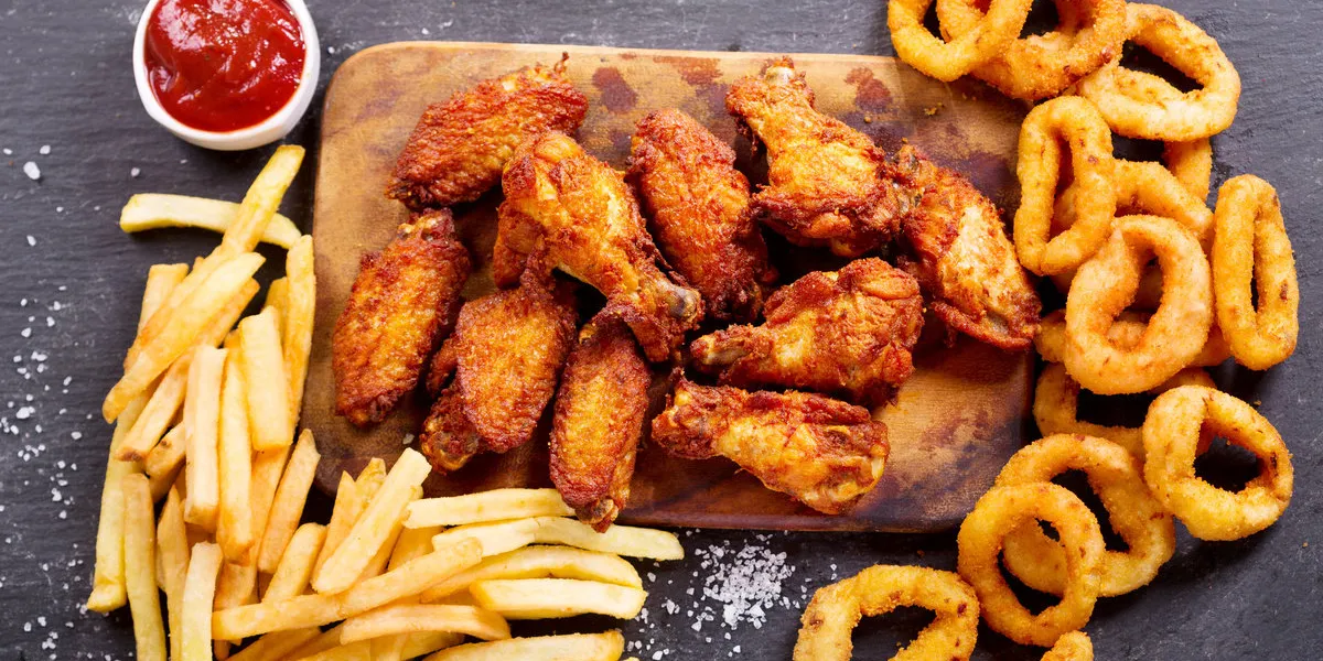 fast food products onion rings, french fries and fried chicken on dark table, top view fast food products onion rings, french fries and fried chicken on dark table, top view