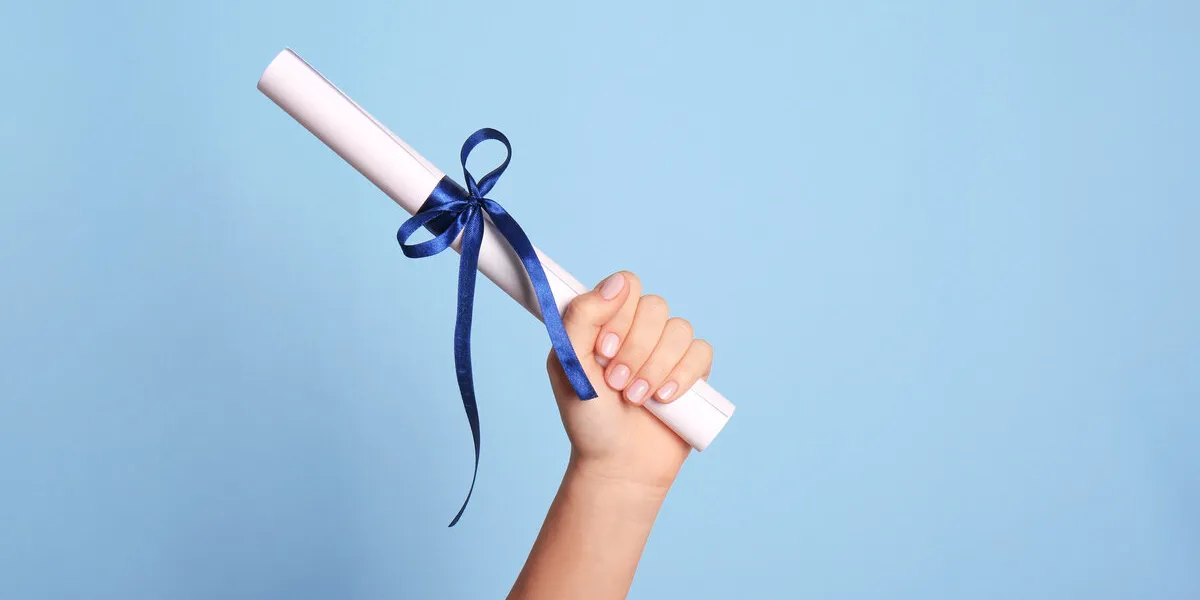 student holding rolled diploma with ribbon on light blue background, closeup