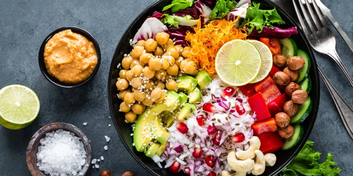 healthy vegetarian buddha bowl with fresh vegetable salad, rice, chickpea, avocado, sweet pepper, cucumber, carrot, pomegranate and nuts closeup