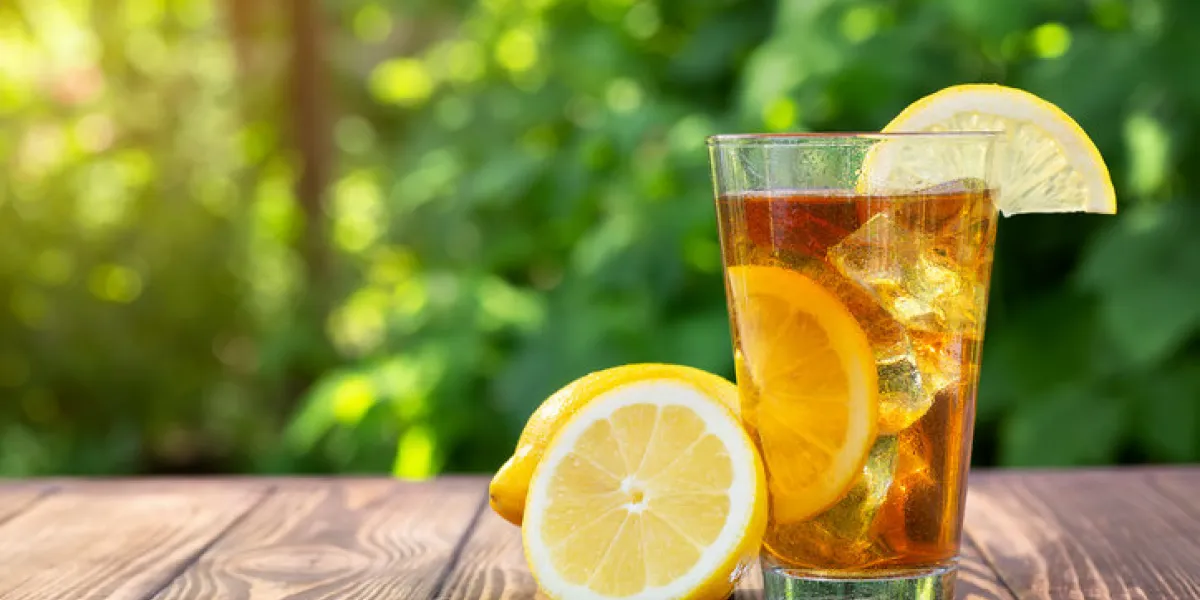 glass of ice tea with lemon on wooden table outdoors