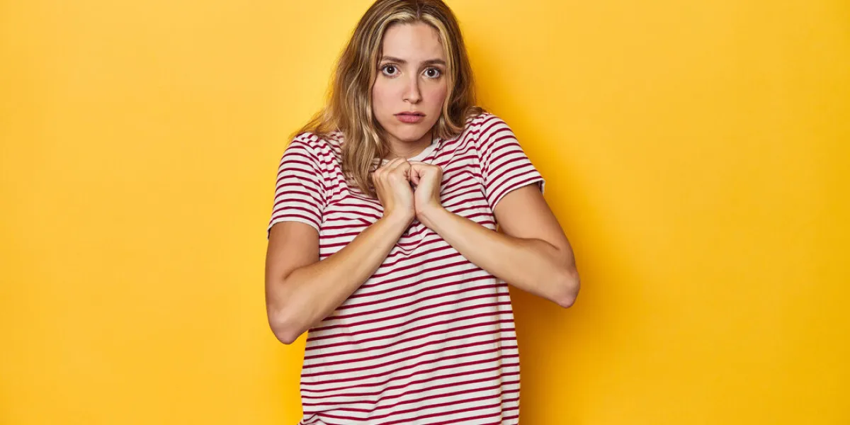 young blonde caucasian woman in a red striped t-shirt on a yellow background, scared and afraid young blonde caucasian woman in a red striped t-shirt on a yellow background, scared and afraid