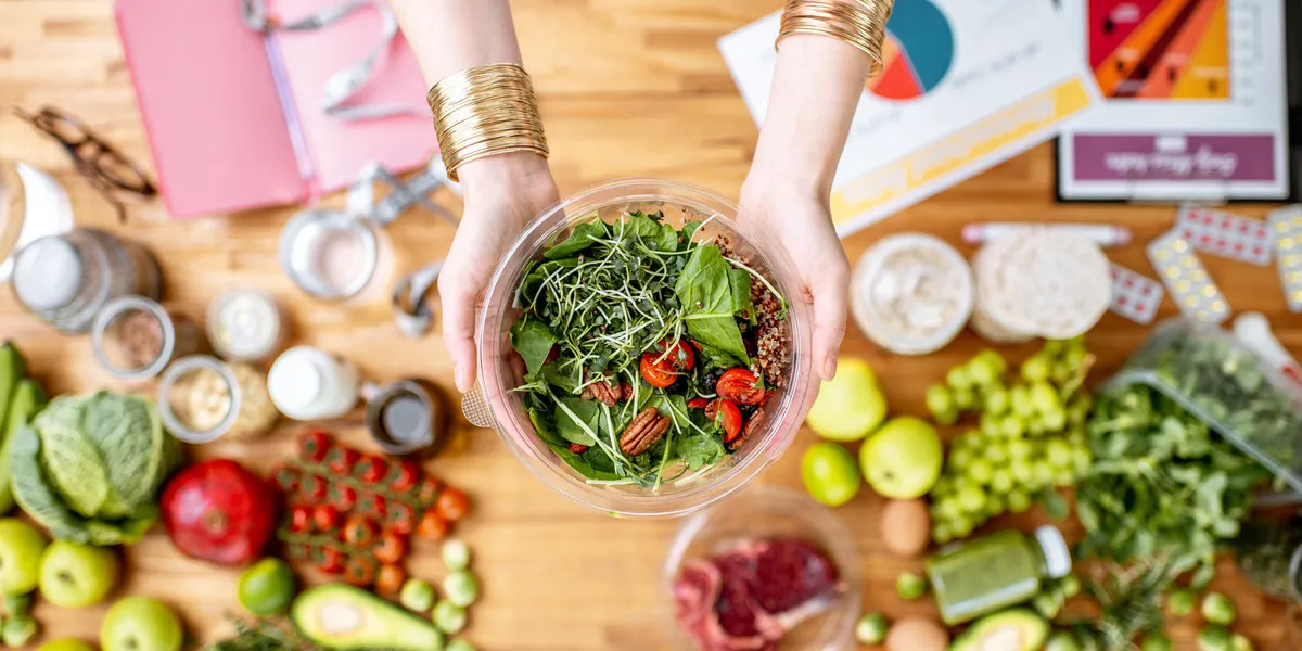 dietitian holding cooked salad above the table full of various healthy products and drawings on the topic of healthy eating dietitian holding cooked salad above the table full of various healthy products and drawings on the topic of healthy eating