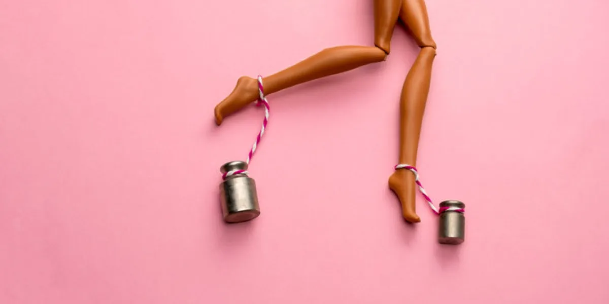 legs of a plastic doll with weights suspended from the ankles, female varicose veins and heaviness in the legs concept on a pink background