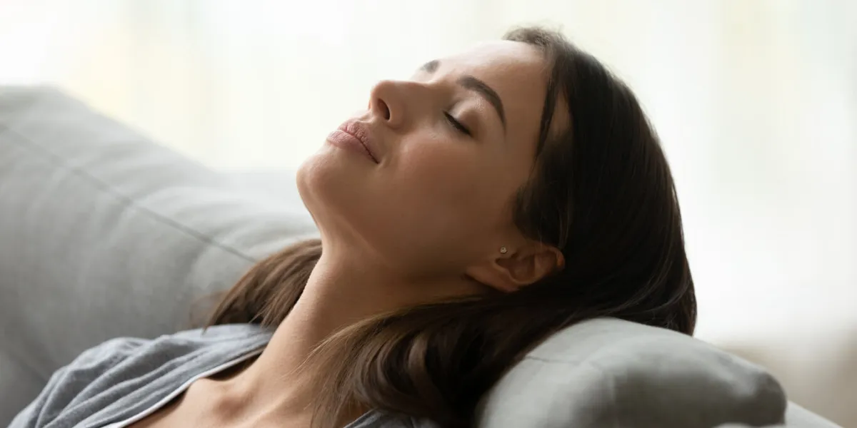 beautiful healthy young woman taking deep breath of fresh air relaxing napping on comfortable couch, attractive calm lady meditating enjoying resting on sofa feel peace of mind at home, close up view