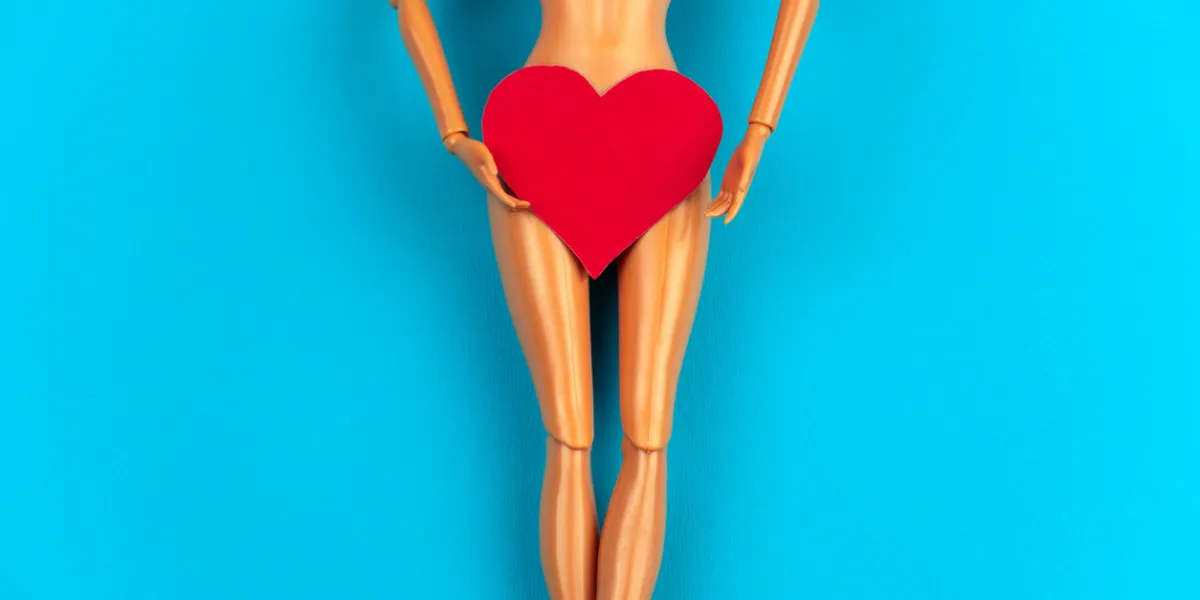legs of a plastic doll with a red heart covering the crotch on a vibrant blue background