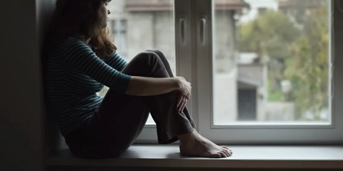 sad young woman sitting on the window, watching out