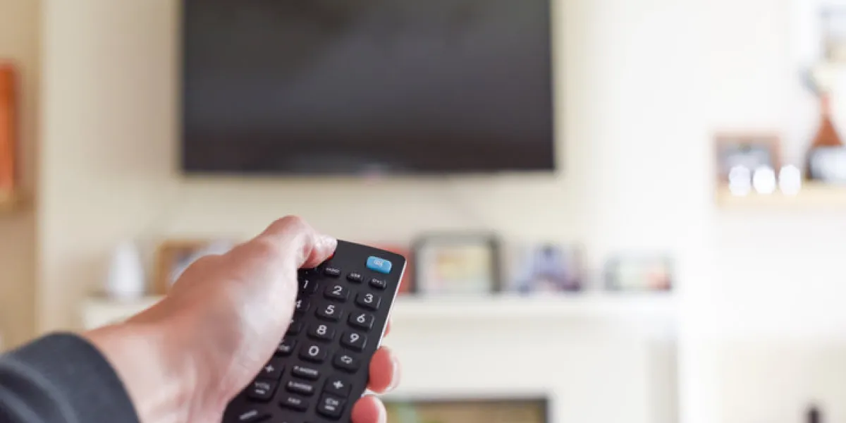 hand with tv remote control switching television on at home