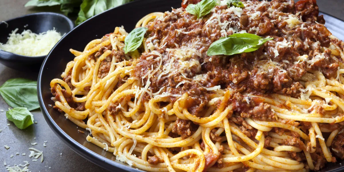 spaghetti bolognese in black serving platter, with fresh basil and parmesan spaghetti bolognese in black serving platter, with fresh basil and parmesan