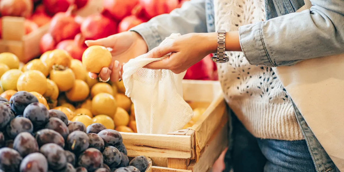 female hands puts fruits and vegetables in cotton produce bag at food market reusable eco bag for shopping sustainable lifestyle eco friendly concept