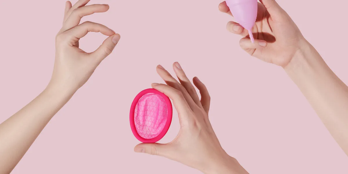 female hands with reusable menstrual disc and cup on pink background female hand making ok sign