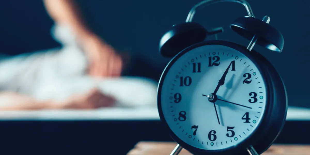 sleeping disorder or insomnia concept, selective focus of vintage clock in bedroom and out of focus male person trying to fall asleep in bed