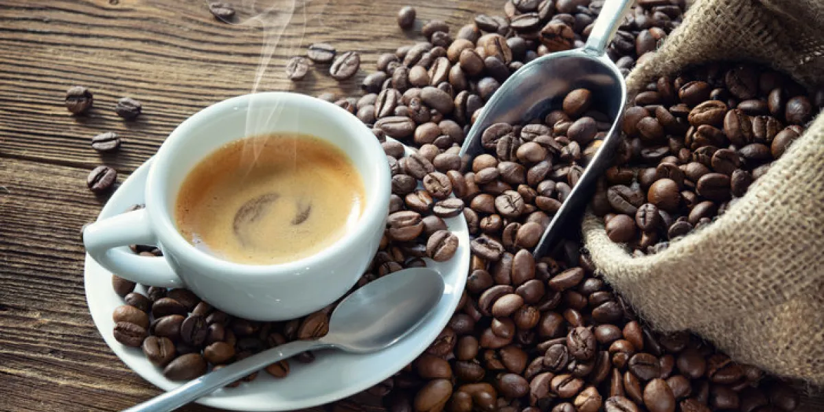 cup of espresso with coffee beans, bag, scoop and steam on rustic wooden background