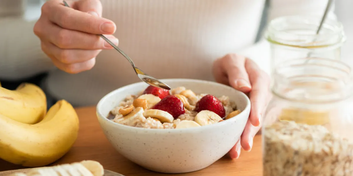 woman eating oatmeal porridge with banana, strawberries and nuts healthy breakfast at the sunny morning kitchen table