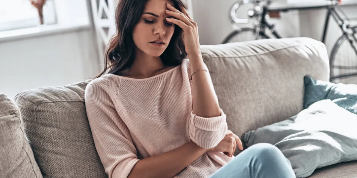 frustrated young woman suffering from the headache while sitting on the sofa at home frustrated young woman suffering from the headache while sitting on the sofa at home