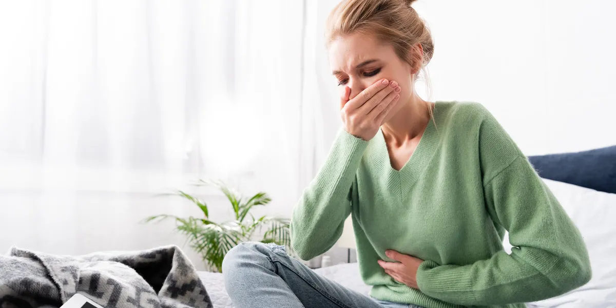 woman having nausea and sitting on bed with digital device woman having nausea and sitting on bed with digital device