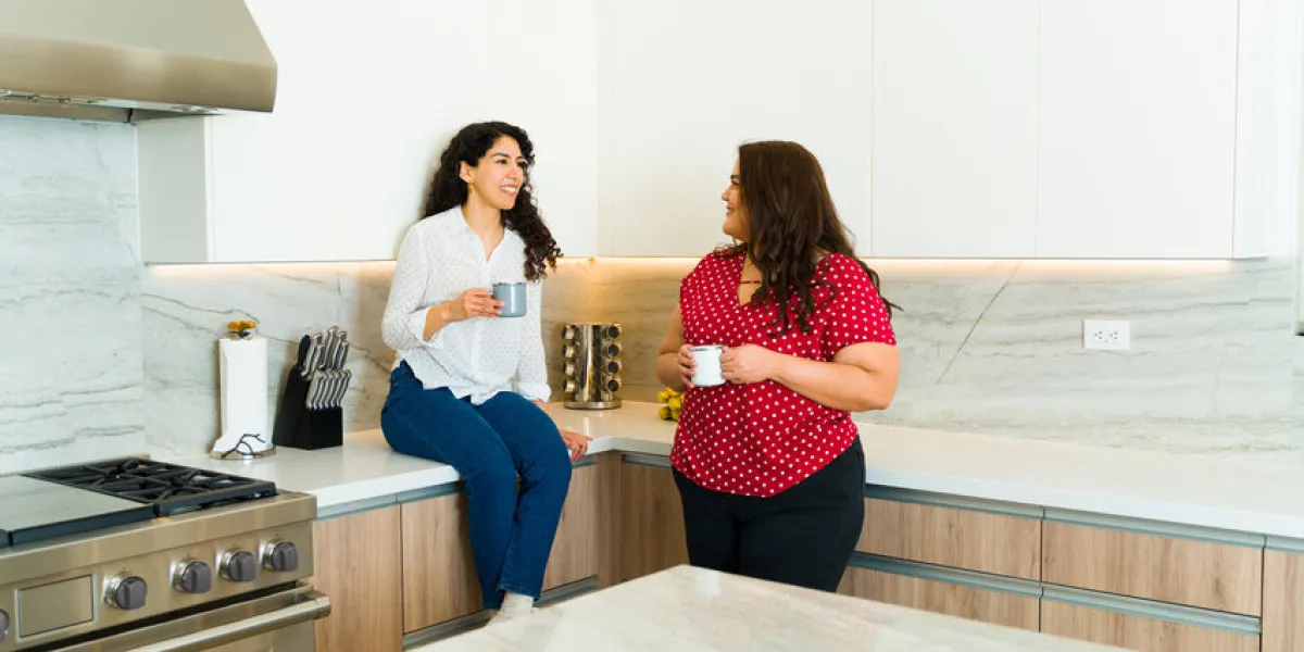 cheerful young women and best friends relaxing while chatting and drinking coffee together in a luxury kitchen cheerful young women and best friends relaxing while chatting and drinking coffee together in a luxury kitchen