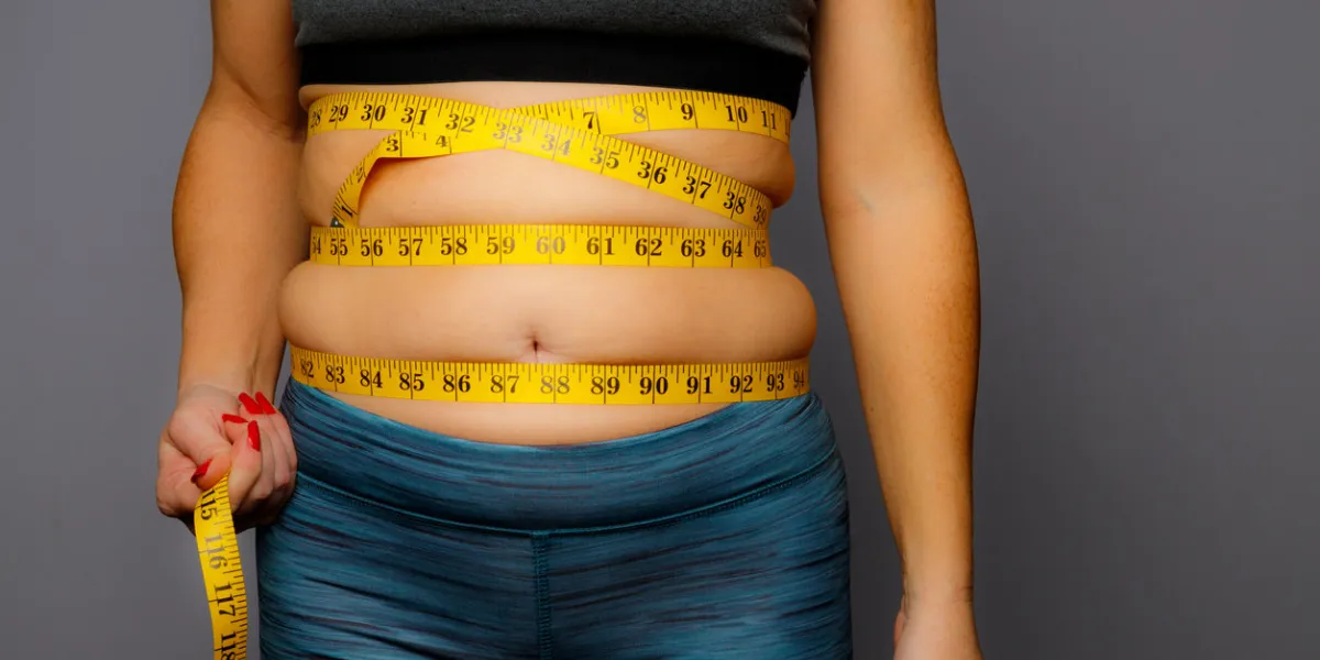 woman in active wear with squeezed measuring tape on a gray backgroundwoman in active wear with squeezed measuring tape on a gray background