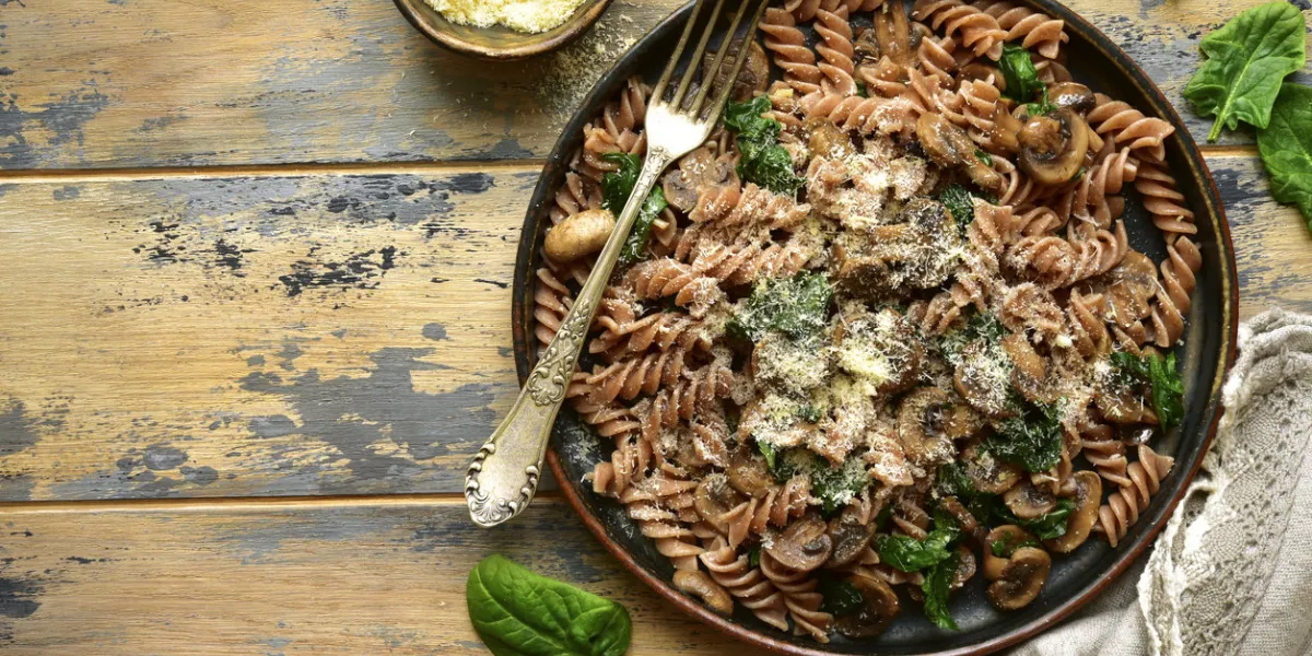 whole wheat fusilli pasta with mushroom and spinach on a dark plate over old rustic wooden backgroundtop view with copy space
