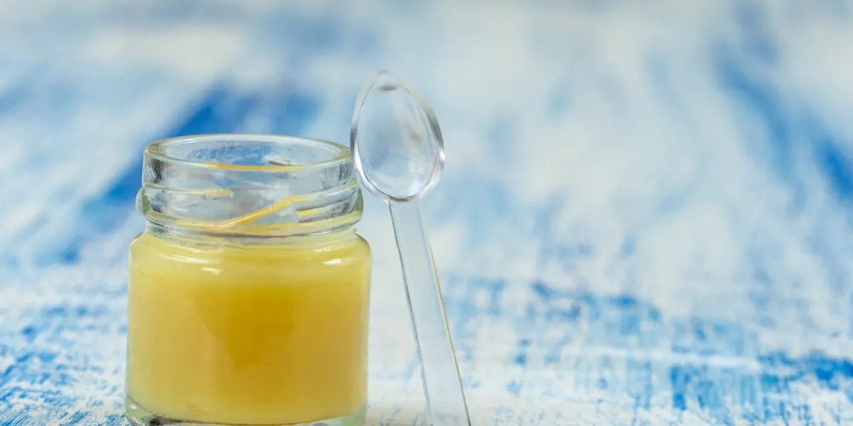 raw organic royal jelly in a small bottle ,royal jelly golden, apiculture over blue ooden background