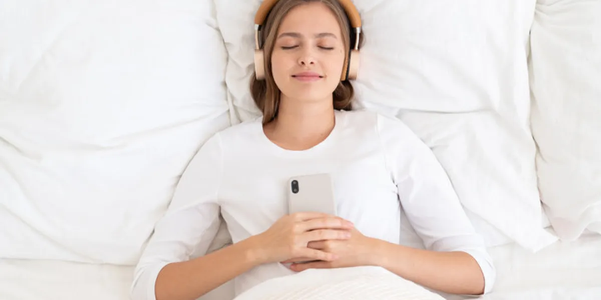 young female dressed in white spending late morning in bed, listening to music or audiobook from her smartphone, dreaming or relaxing young female dressed in white spending late morning in bed, listening to music or audiobook from her smartphone, dreaming or relaxing
