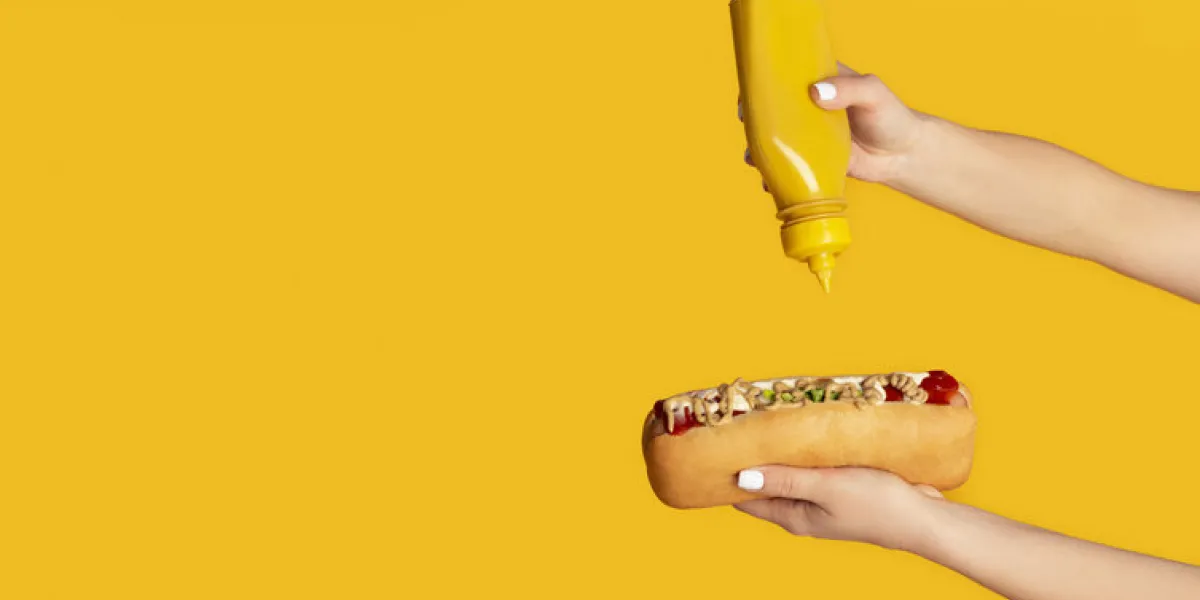 unrecognizable woman squeezing mustard onto hot dog against orange background, blank space panorama unrecognizable woman squeezing mustard onto hot dog against orange background, blank space panorama