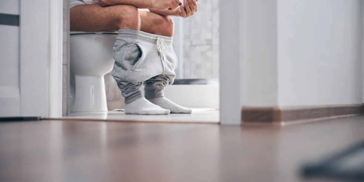 cropped photo of a caucasian male with a cellular phone sitting on the toilet seat