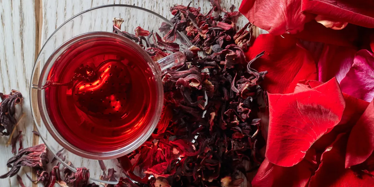 red hot hibiscus tea in a glass mug on a wooden table among rose petals and dry tea custard with metallic heart