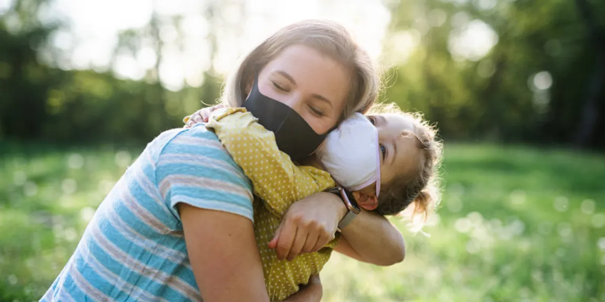 side view of happy mother hugging small daughter on trip in nature, wearing face masks