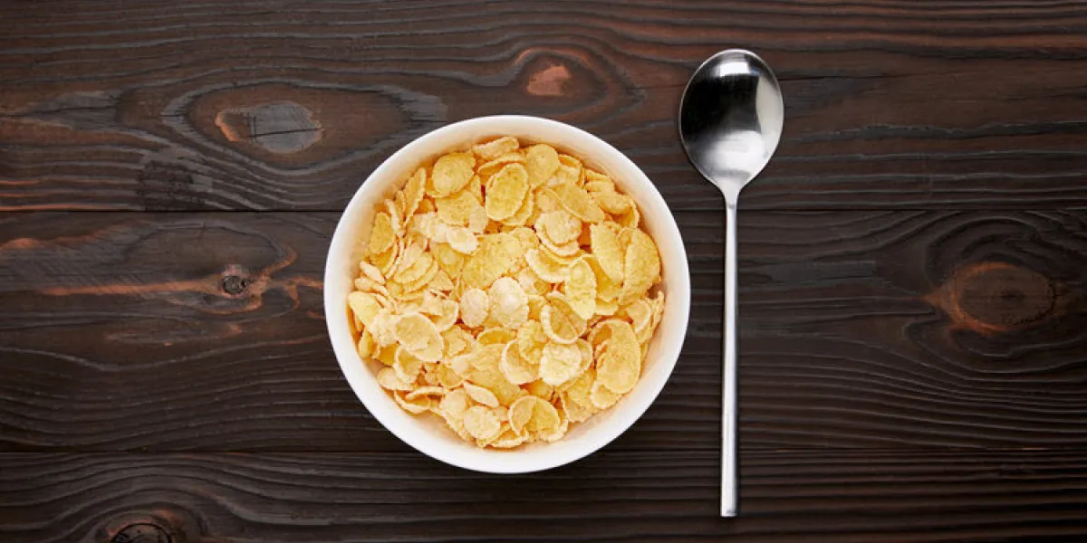 top view of spoon near cornflakes in bowl on wooden surface
