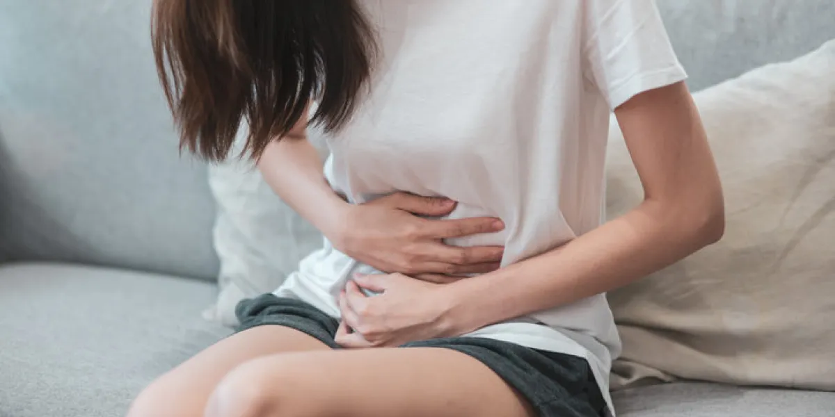 healthcare medical or daily life concept   close up stomach of young lady have a stomachache or menstruation pain sitting on a sofa