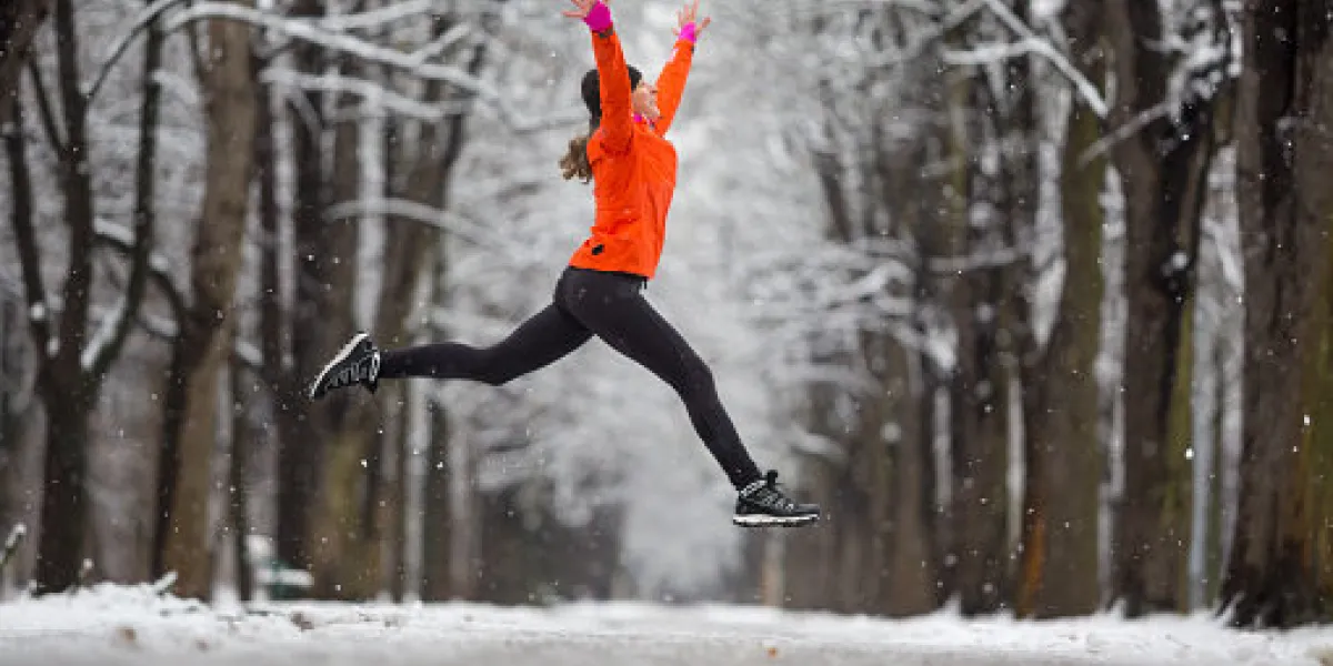 active woman in running outfit jumping during snowfall in winter december in alley snow on road and trees cold bad weather active woman in running outfit jumping during snowfall in winter december in alley snow on road and trees cold bad weather