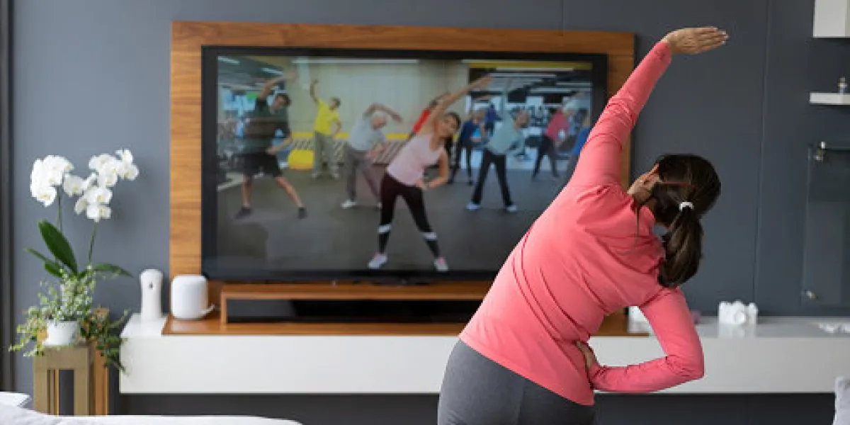 back view of senior woman following an online stretching class looking at tv screen - technology concepts image on screen belongs to us
