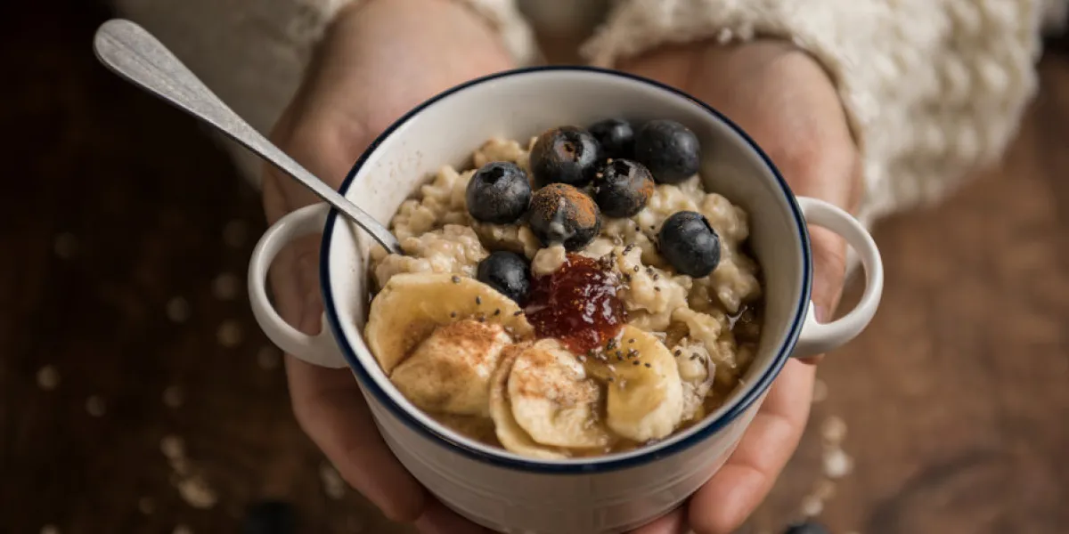 woman hands offering a vegan porridge with oat flakes, banana, blueberries, chia, cinnamon, maple syrup and strawberry jam horizontal top view woman hands offering a vegan porridge with oat flakes, banana, blueberries, chia, cinnamon, maple syrup and strawberry jam horizontal top view