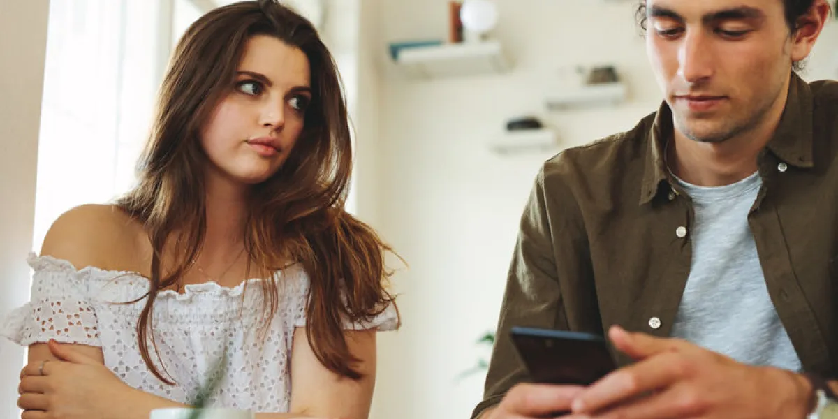 woman looking unhappy while her man paying no attention to her and busy using his mobile phone sulking woman sitting next to man reading text messages during a date woman looking unhappy while her man paying no attention to her and busy using his mobile phone sulking woman sitting next to man reading text messages during a date