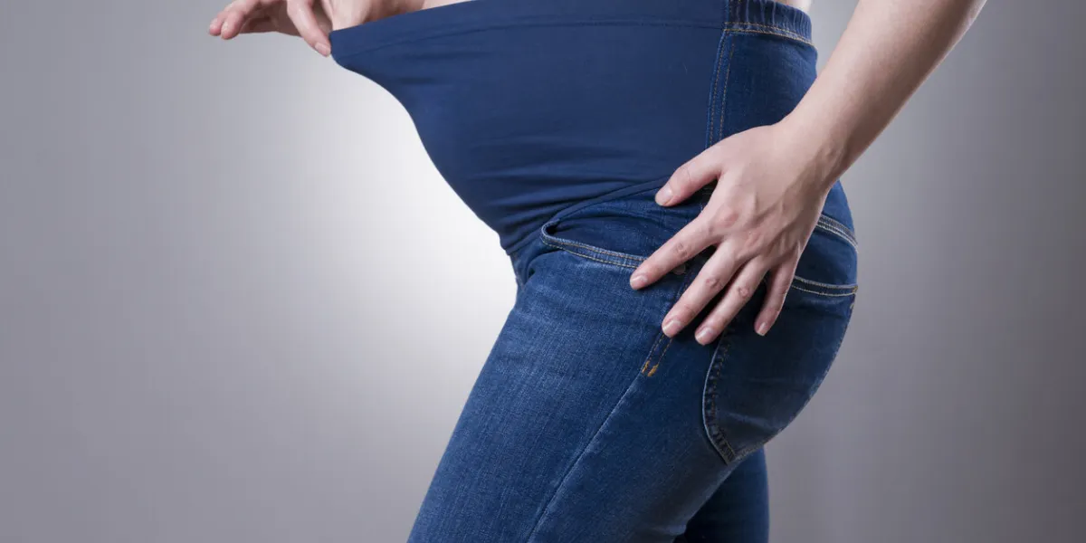 pregnant woman in blue jeans for pregnant women on gray background side view