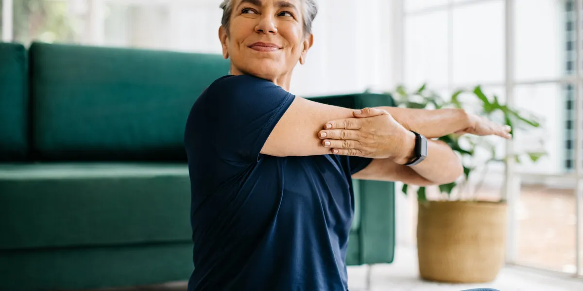 happy and healthy senior woman doing a cross arm stretch in a peaceful yoga session at home happy and healthy senior woman doing a cross arm stretch in a peaceful yoga session at home