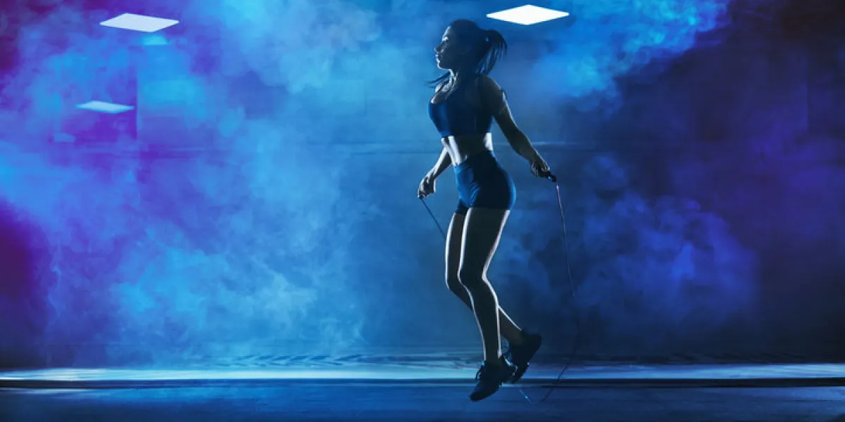 side view of pretty female bodybuilder in sport suit with perfect body using skipping rope in gym young athletic woman jumping in hall, dark atmosphere with smoke and backlit concept of sport side view of pretty female bodybuilder in sport suit with perfect body using skipping rope in gym young athletic woman jumping in hall, dark atmosphere with smoke and backlit concept of sport
