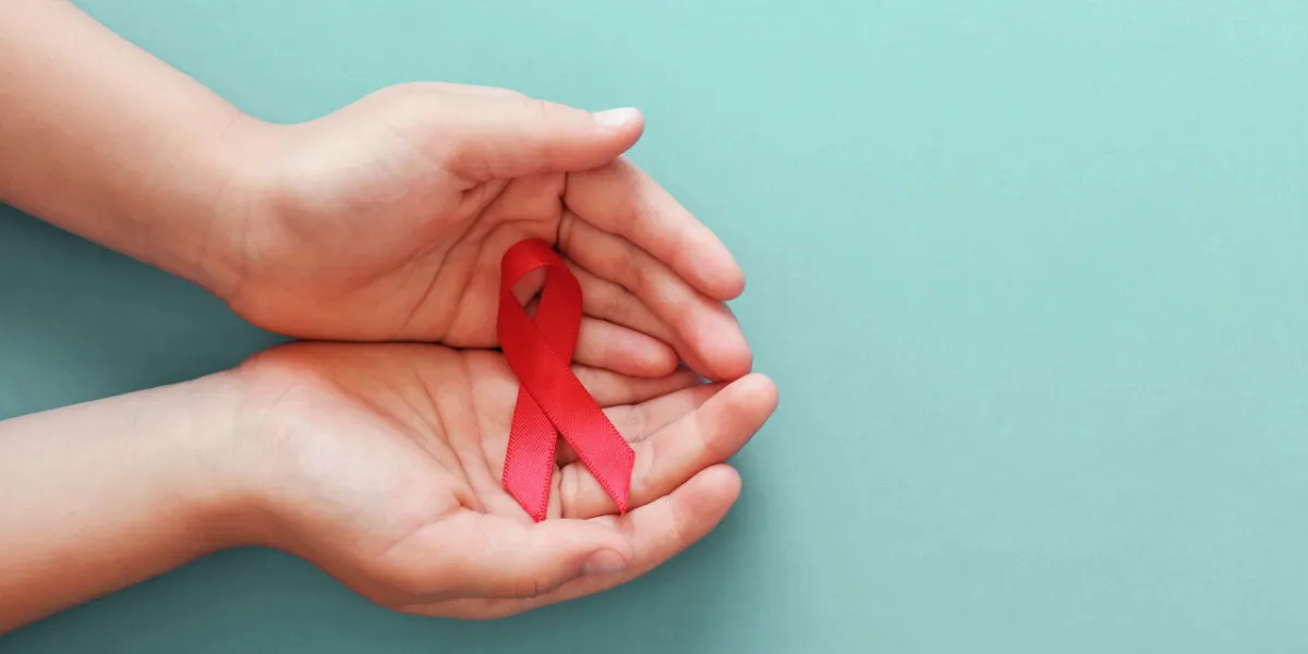 hands holding red ribbon on blue background, hiv awareness concept, world aids day, world hypertension day