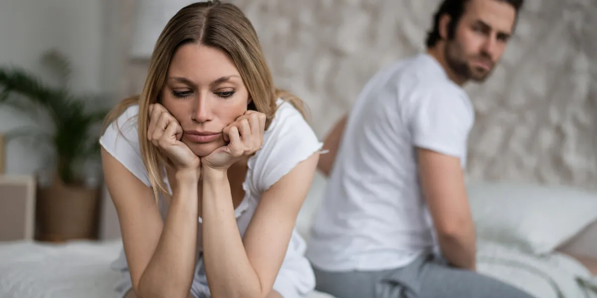 sexual problems, relationship crisis concept stressed young woman sitting on bed, overwhelmed with family difficulties, her offended husband on background, blank space sexual problems, relationship crisis concept stressed young woman sitting on bed, overwhelmed with family difficulties, her offended husband on background, blank space