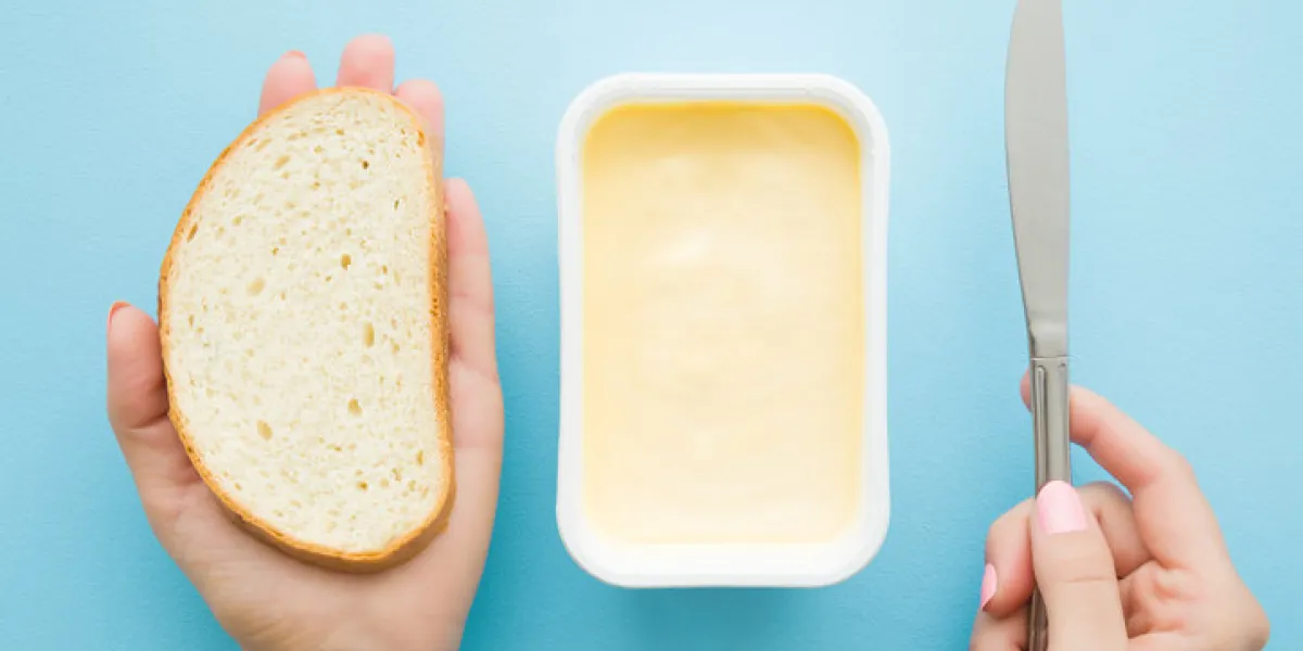 woman's hands holding slice of white bread and knife opened plastic pack of light yellow margarine on pastel blue desk preparing breakfast point of view shot closeup top view woman's hands holding slice of white bread and knife opened plastic pack of light yellow margarine on pastel blue desk preparing breakfast point of view shot closeup top view