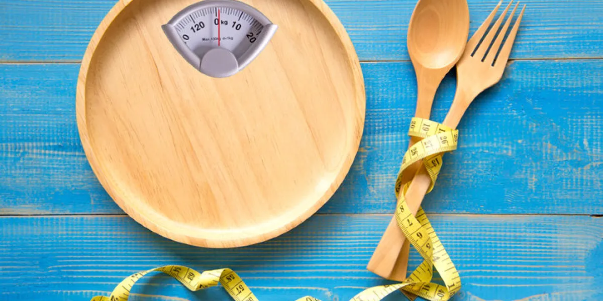 scale shaped on the wood plate with a fork and spoon, blue background diet and healthy concept scale shaped on the wood plate with a fork and spoon, blue background diet and healthy concept