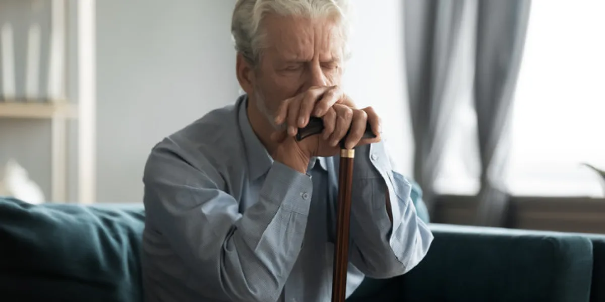 depressed disabled retired elderly 50s grandfather hold in hands walking stick sit alone on couch looking lonely and unhappy, health problems, physically handicapped person, movement disorder concept
