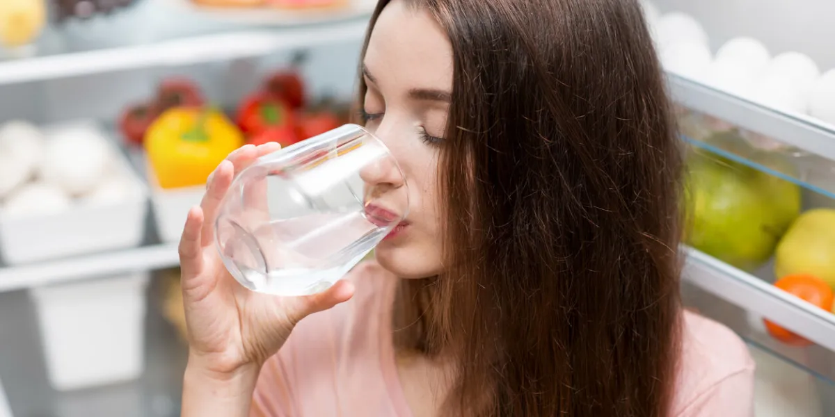young woman drinking water near the refrigerator