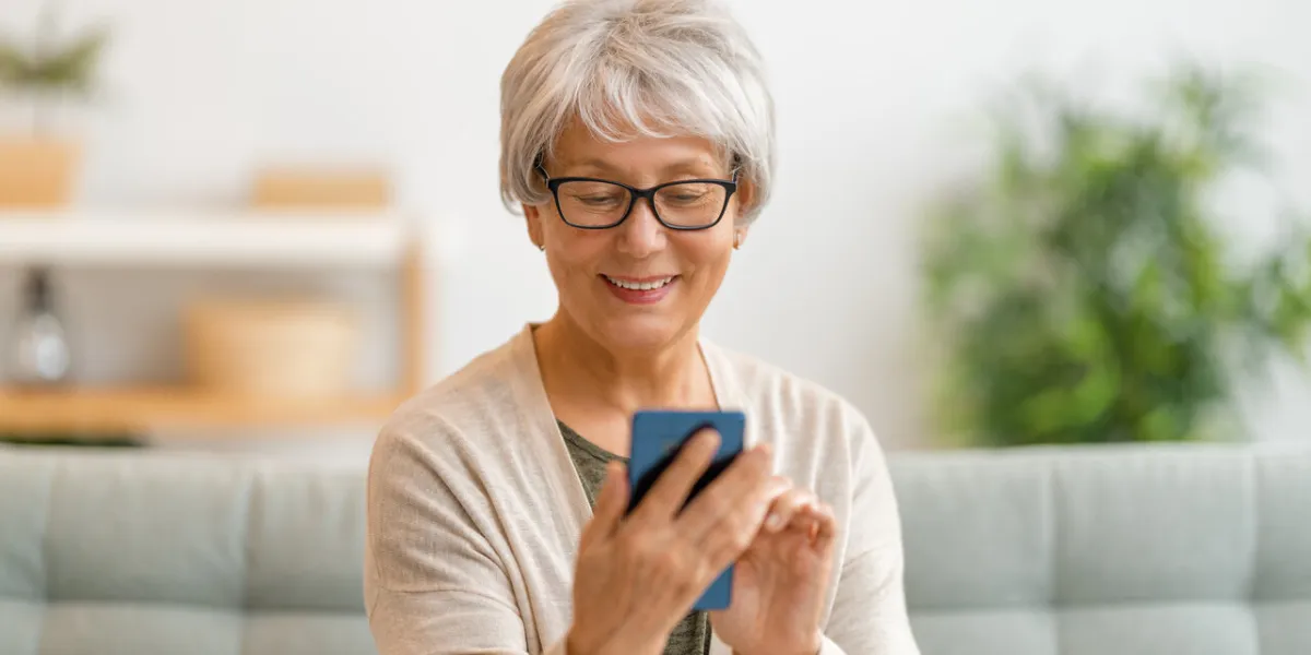 joyful beautiful senior woman is using smartphone sitting on the sofa at home
