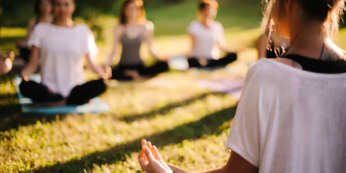 group of young sporty woman practicing yoga lesson with instructor, sitting in lotus pose focus of camera at teacher rear view photo from back of instructor group of meditating people in background