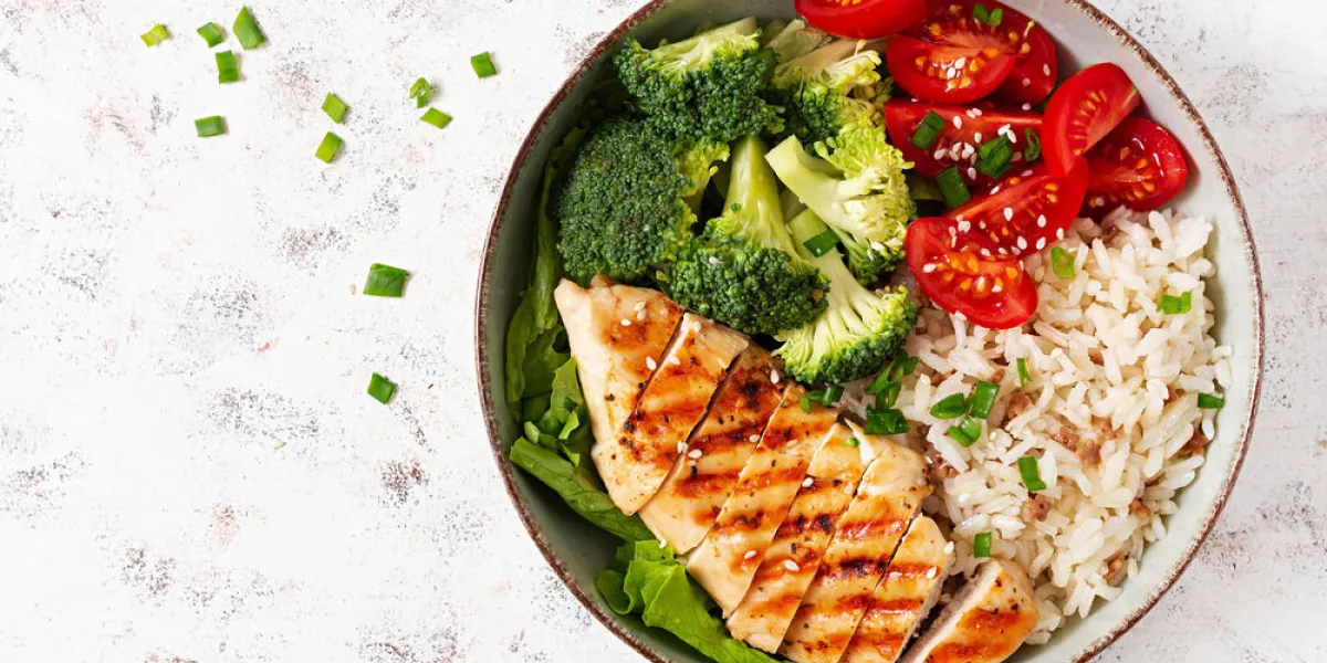 delicious buddha bowl with grilled chicken, fresh vegetables and rice on a light background top view, above delicious buddha bowl with grilled chicken, fresh vegetables and rice on a light background top view, above