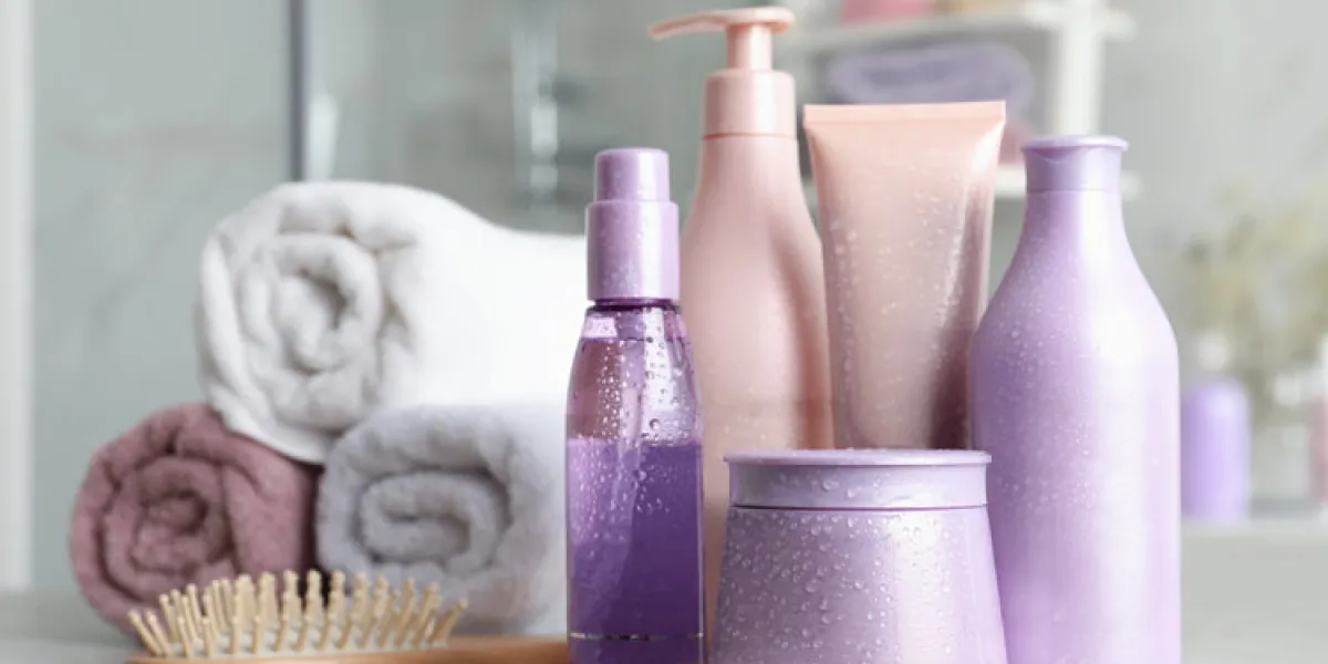 set of hair care cosmetic products covered with water drops on light grey stone table in bathroom