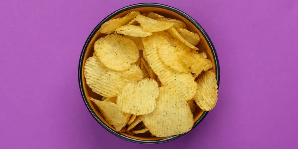 bowl with ribbed chips on purple background top view